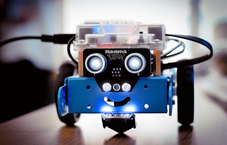Dečak za računarom, pored njega mBot robot na stolu