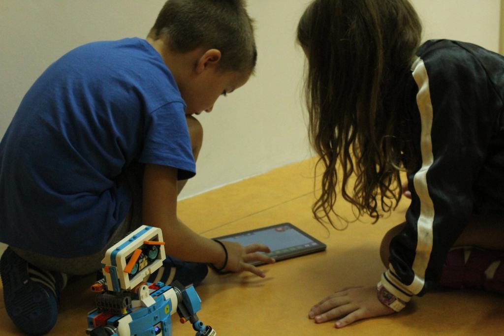 Dvoje dece na podu prati robota koji se kreće