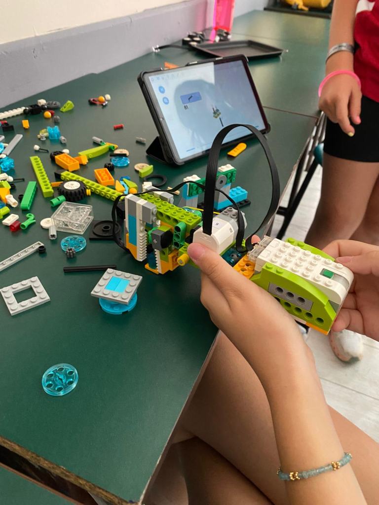 Dete drži sklopljenog LEGO robota, na stolu su delovi i tablet sa uputstvom
