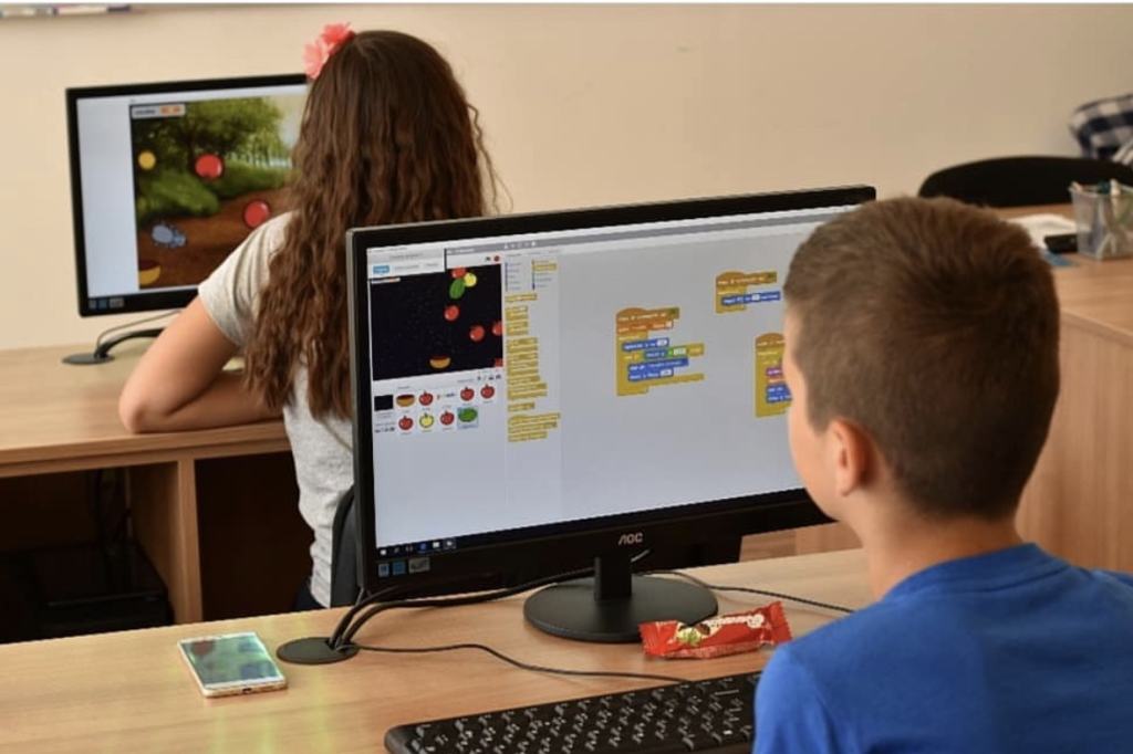Devojčica i dečak za stonim računarima, na ekranu je projekat u Scratch-u