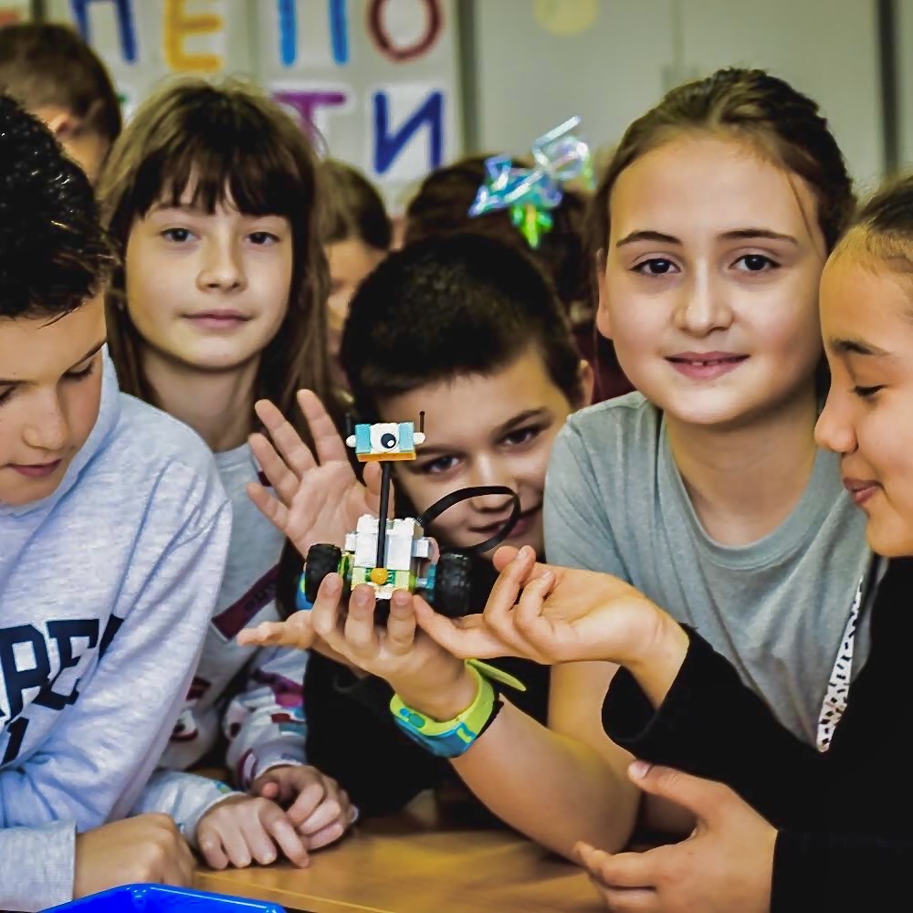 Grupa dece u učionici, jedan dečak drži sklopljenog LEGO robota